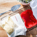 Load image into Gallery viewer, A collection of ingredients for red velvet cake: flour, cocoa, sugar, eggs, buttermilk, and red dye